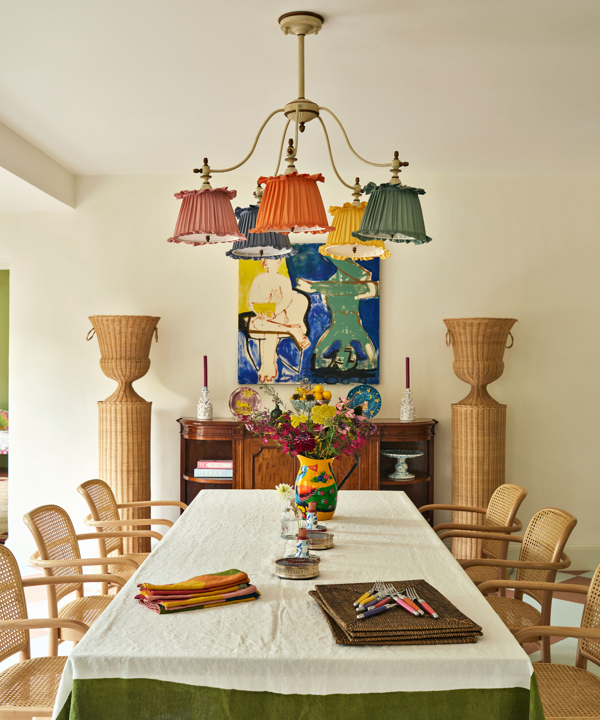Airy dining room featuring cane dining chairs, wicker urns, a multicolor, multi shade chandelier, and colorful artwork