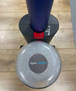 Closeup of the Dyson WashG1's clean water tank, full with soapy water with 'Dyson WashG1' logo on top, on wooden floor in Future test center