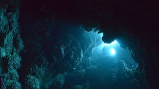 Light shines through the water of a rocky cave in the deep sea.