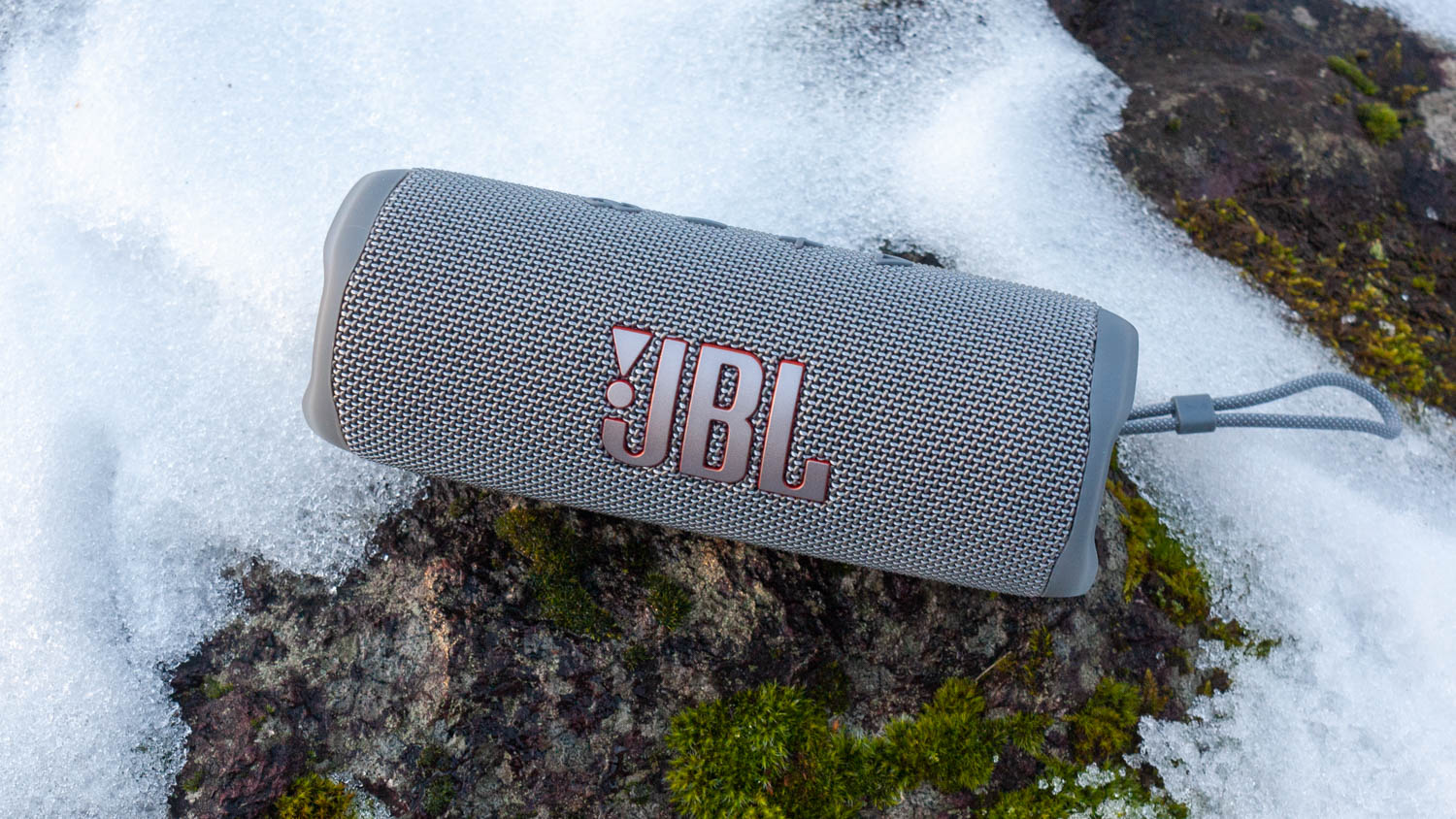Bluetooth-høyttaleren JBL Flip 6 i grått, liggende ute i snøen.