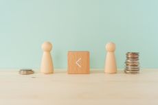 two wooden block people set up beside stacks of coins with wooden block and greater than symbol separating them