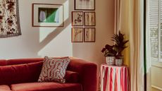A living room with a red couch, a gallery wall and a striped tablecloth on a side table with potted plants