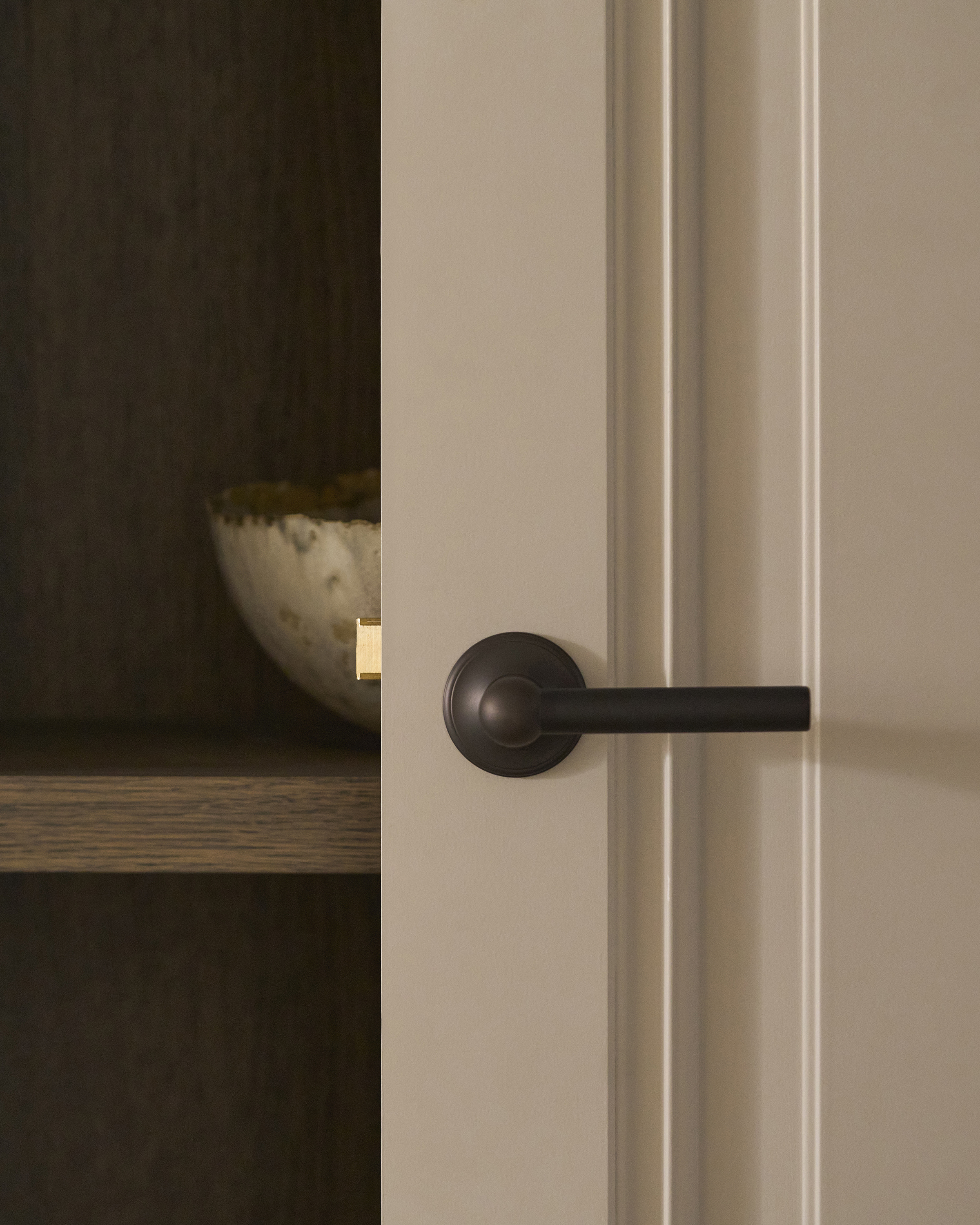 a dark bronze door handles on a beige door looking into an open cupboard