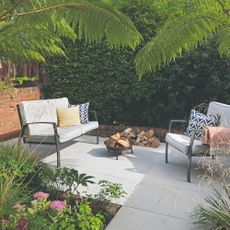 A paved patio with a 2-seater outdoor sofa and a matching chair with a small fire pit in the middle