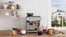 The Breville Barista Express espresso machine on a wooden worktop with white tiles and a window.