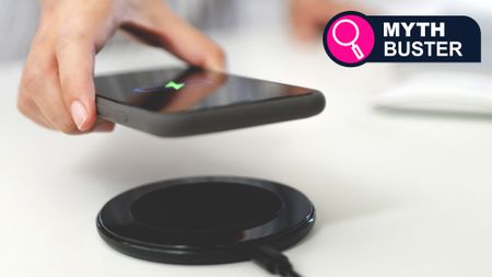 A hand holding a phone above a wireless charger
