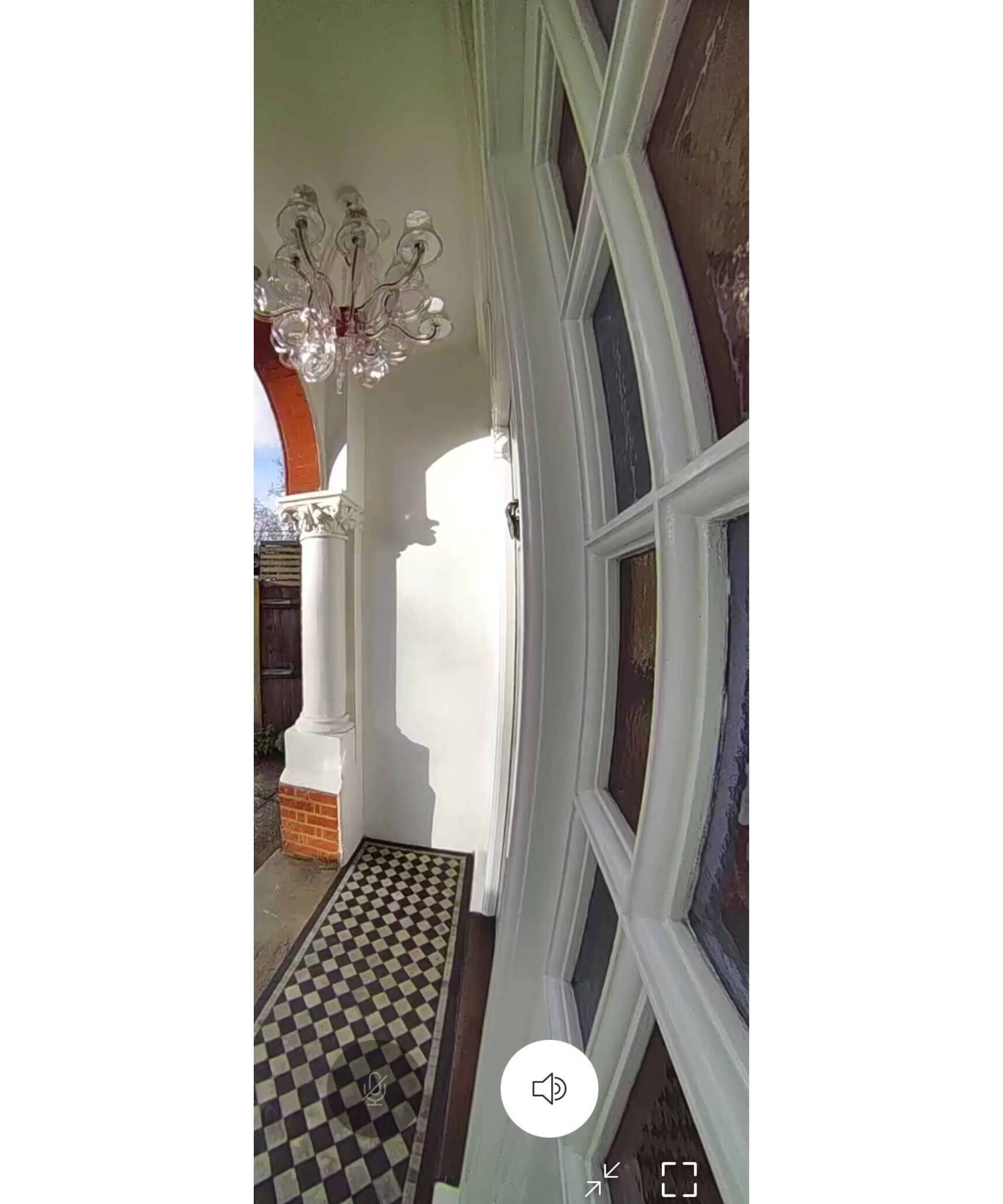 The view from a Ring Battery Doorbell Pro of a porch with stained glass windows to the right, a black and white tiled floor, and a clear chandelier hanging above.
