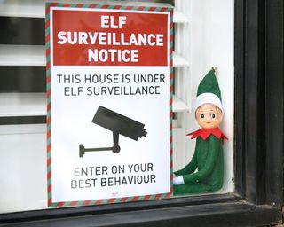 An elf toy sitting by the window with an A4 elf surveillance notice