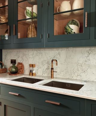 marble splashback and worktop, brass textured handles on green and glass cabinets