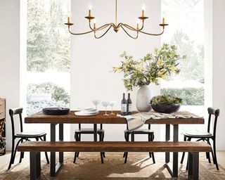 Light and bright dining room with white walls, large windows, large wooden dining table with bench and chair seating, low hanging metal chandelier