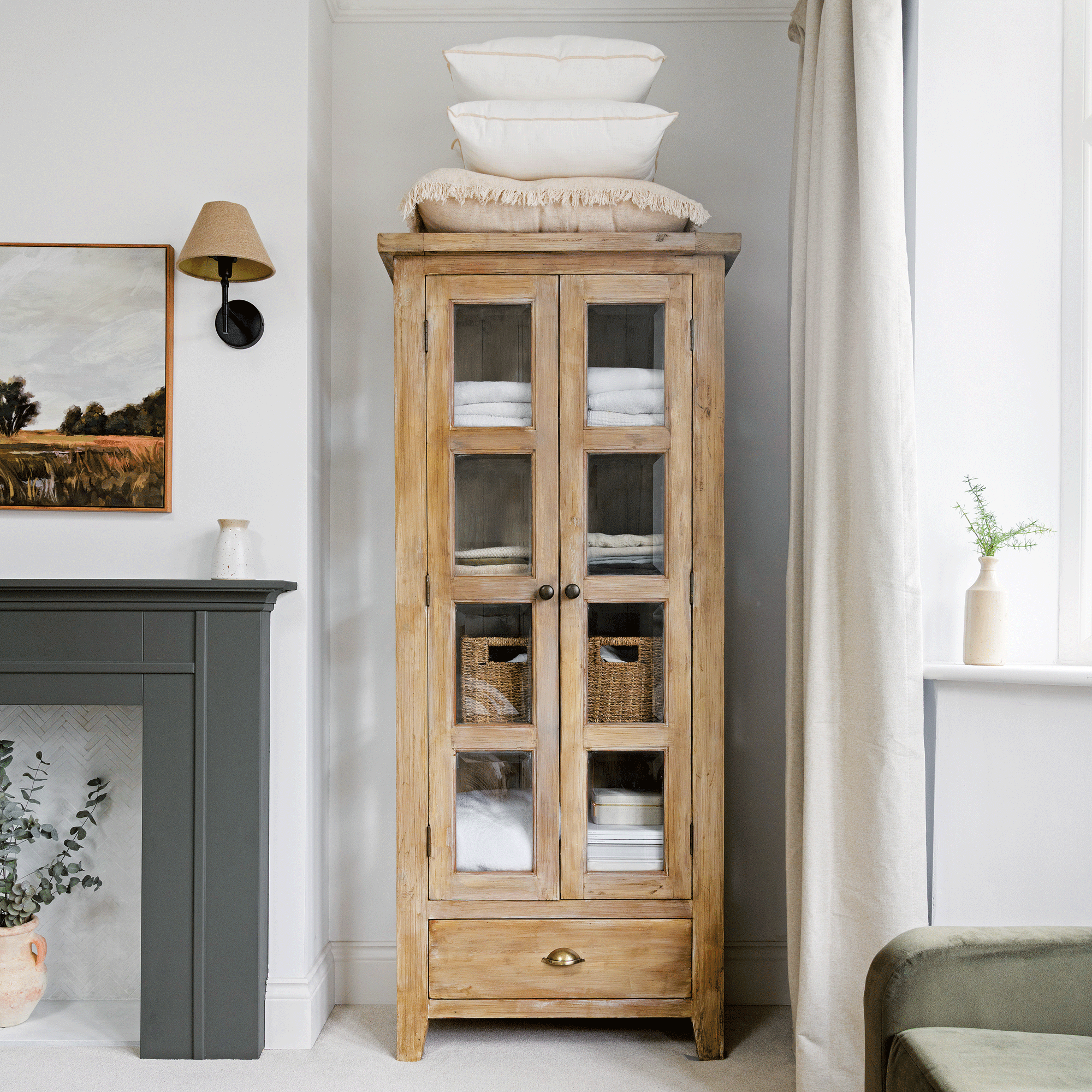 a bedroom with a tall glass-fronted cabinet filled with spare bedding and baskets