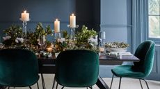 Christmas table setting with dark green chairs and greenery and candles on the table