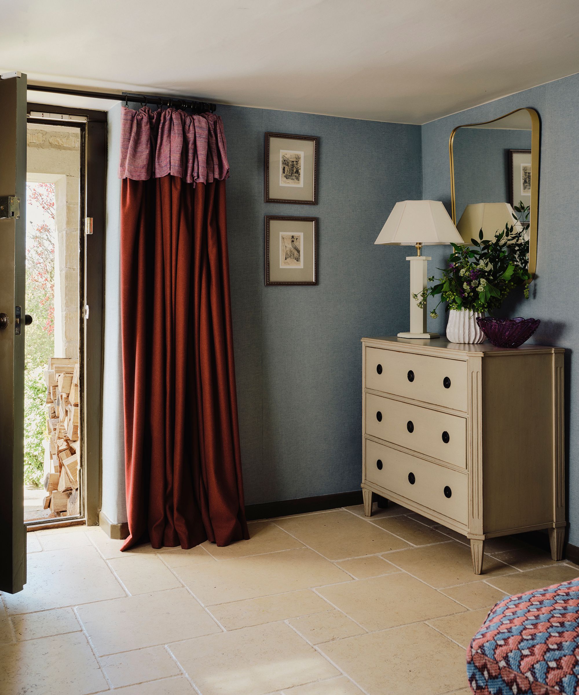 blue small entryway with a green front door and a red velvet frill curtain hung at the door with a chest of drawers, lamp, mirror, and vase
