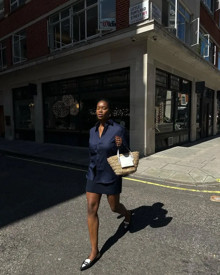 A woman wearing a navy and skirt, and black and white backless loafers