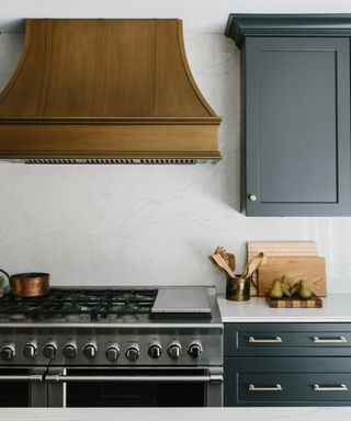 A kitchen with white marble splashback, black cabinets and a bronze hood
