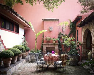 apartment patio with rose painted walls, wrought iron table and chairs, pots of plants, urns