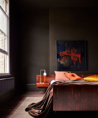 Brown bedroom with orange pillows, brown painted walls and wood flooring