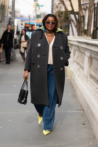 A woman at Fashion Week in a long coat and trousers