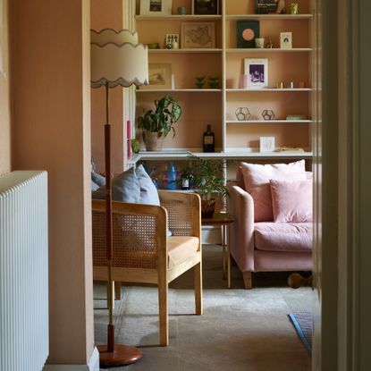 A peach-painted living room with a pink velvet sofa and a floor lamp with a scalloped shade