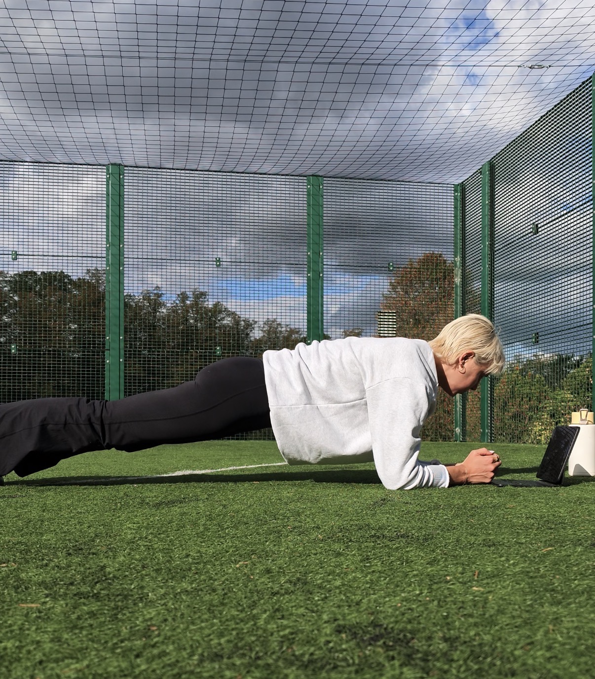 A side profile of a woman practicing a forearm plank on green astroturf