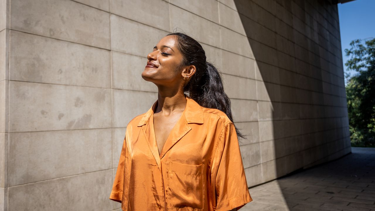 Best glowy sunscreens woman wearing orange shirt looking into the sun looking glowy