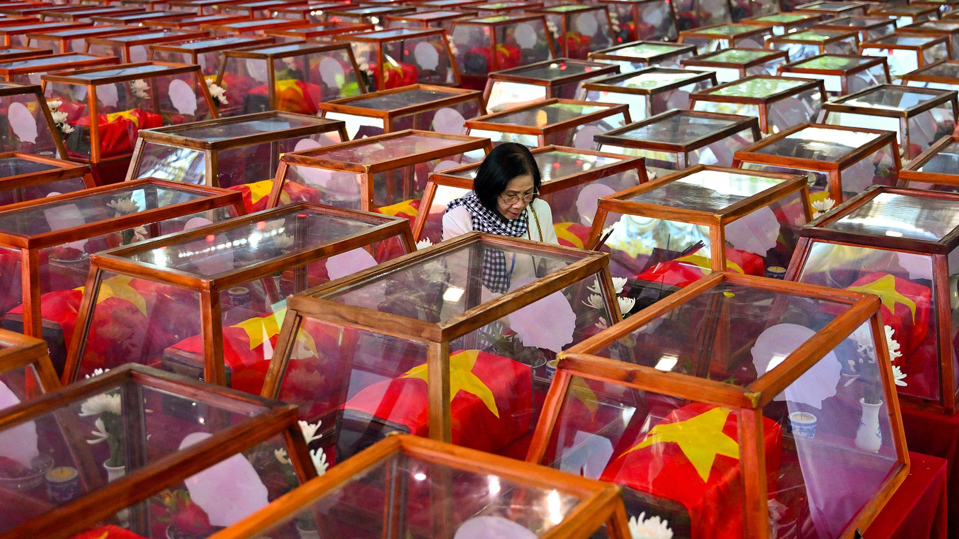 A woman stands beside caskets bearing the remains of fallen soldiers at Lê Thị Riêng Park in Ho Chi Minh City, Vietnam. Funeral rites for more than 700 war dead were held in an effort to identify those missing from decades of conflict