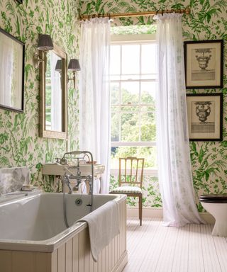 An example of ensuite ideas showing a bathroom with green, plant print wallpaper, a large bath and a window