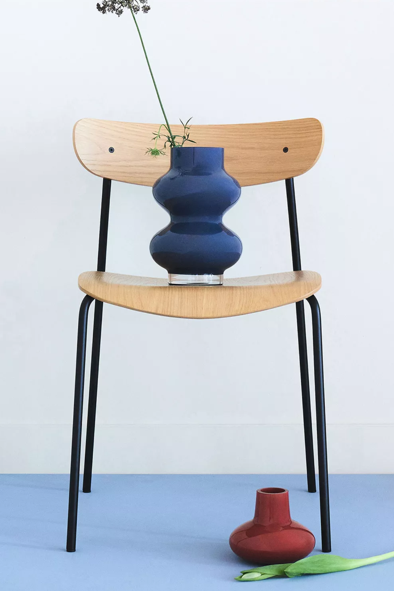 A blue wavy vase on a chair with a red vase below