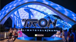 People walking around the Tron Lightcycle Run attraction entrance at night.
