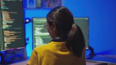 Female software developer coding in Python and JavaScript with code pictured on desktop computer screens in a home office.