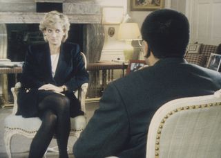 Princess Diana wearing a black skirt suit and tights sitting in a chair talking to Martin Bashir