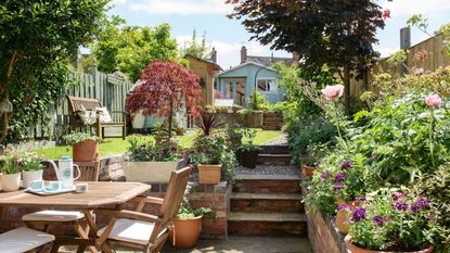 Patio garden with wooden garden furniture, steps leading to lawn area, and a blue shed at the bottom of the garden 