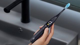 A person holding a black Oclean X Ultra S sonic electric toothbrush