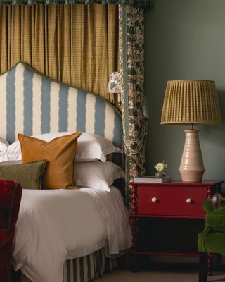 A traditional bed with yellow textiles behind the blue and cream striped headboard with a bold yellow accent throughout