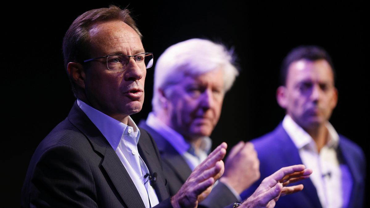 BT Group CEO Philip Jansen, standing with his hands raised. Behind him, BT CMO Gerry McQuade and head of consumer unit at BT Marc Allera are looking at him, slightly out of focus.