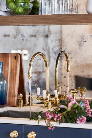 mirrored splashback behind sink with gold tap and navy cabinetry