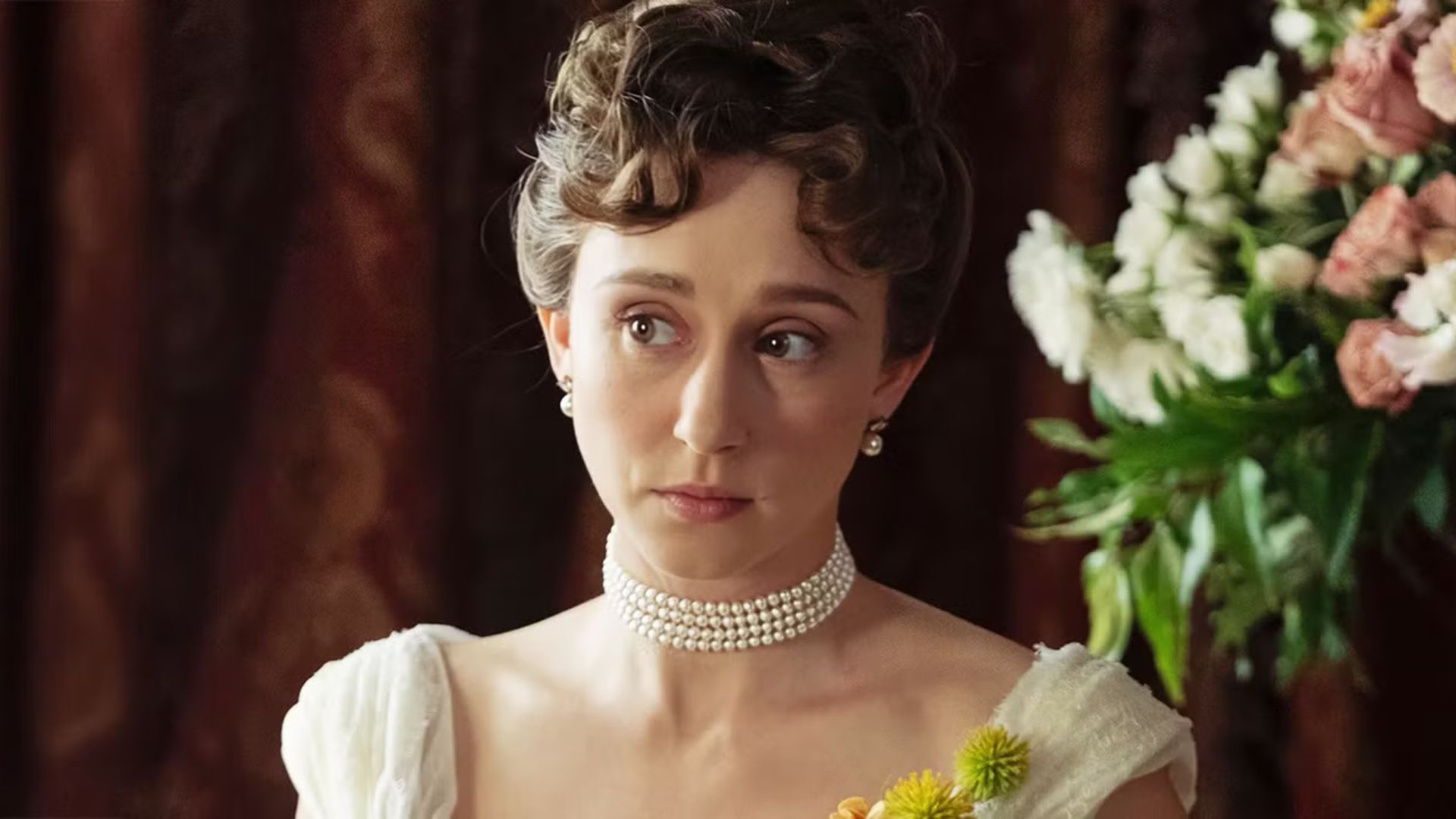 Gladys looks to her right while sat by a bouquet of flowers