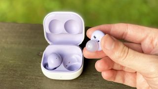 the samsung galaxy buds 2: one in the case, and one being held between the thumb and forefingere