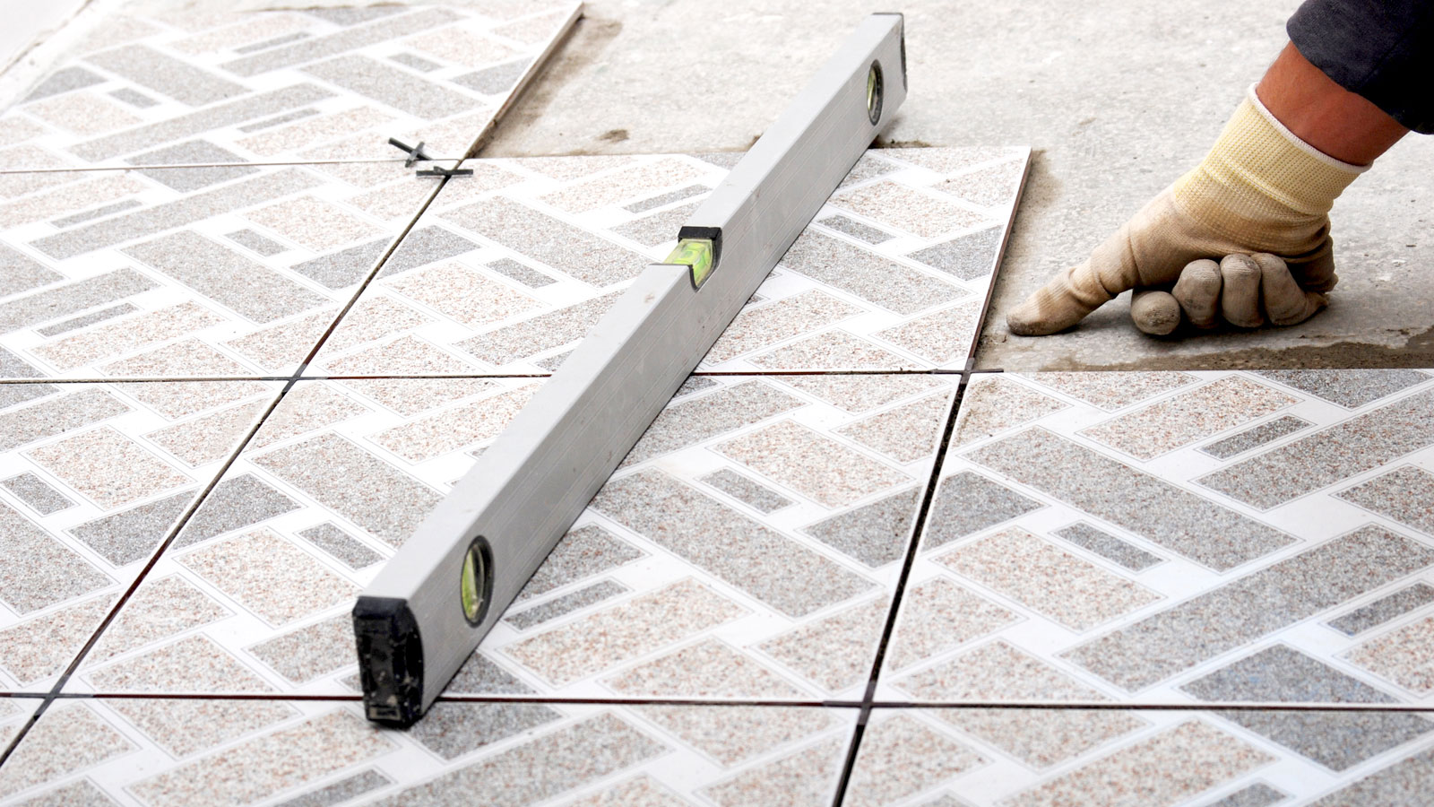 Silver spirit level on top of abstract pastel ceramic tiles with bar floor in background