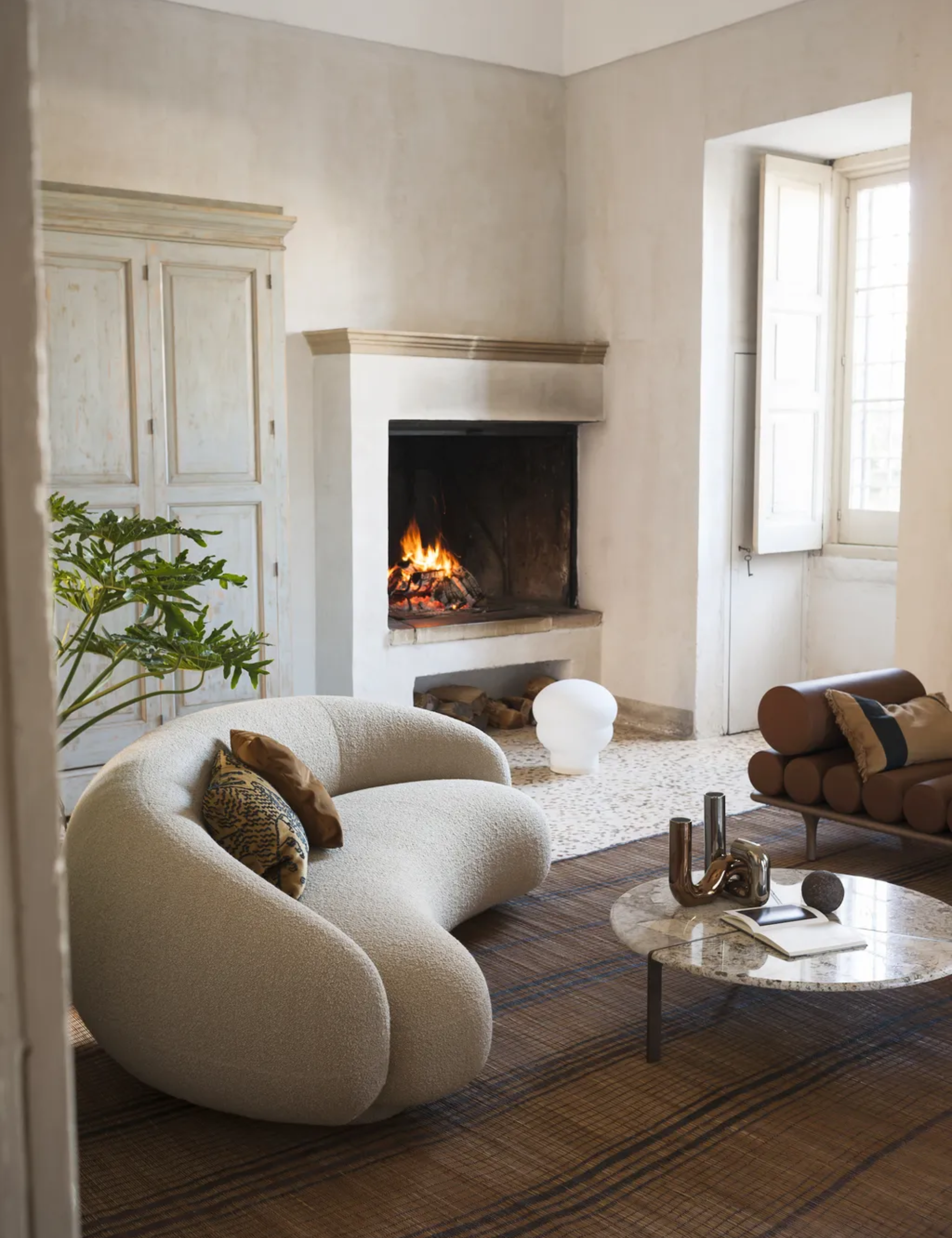 neutral living room with plaster walls, open fire, modern boucle couch, textured rug, shutters, leather couch, marble round coffee table