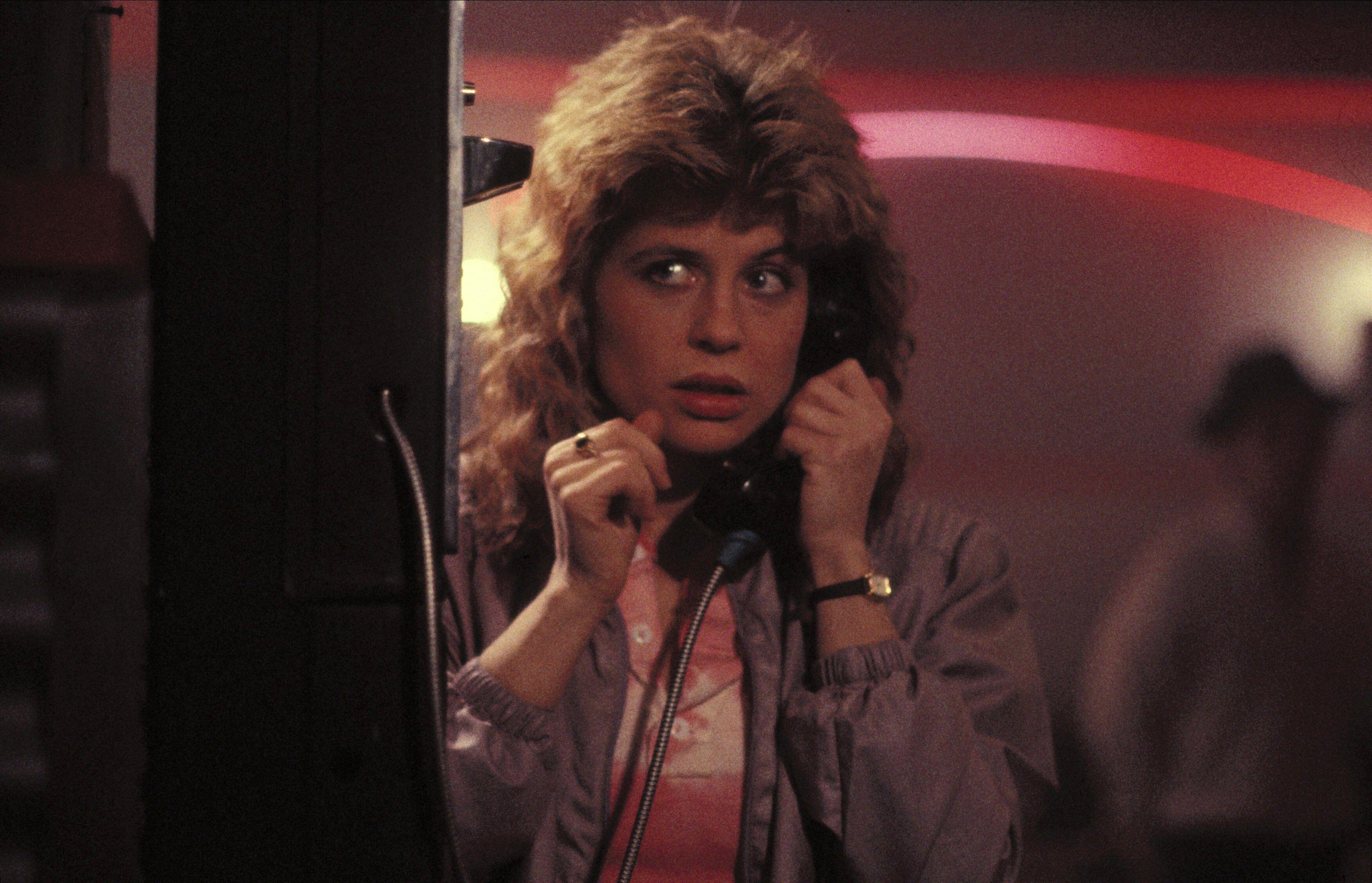 linda hamilton as sarah connor looking scared and talking on a pay phone at a club in the terminator 1984