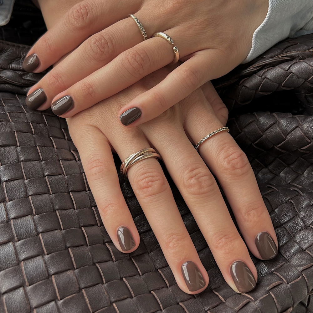 A pair of hands on a woven brown bag wearing a chocolate brown nail colour