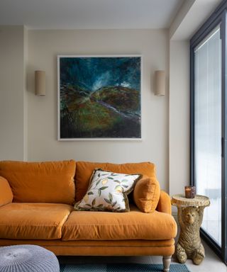 A beige room with an orange couch and hanging artwork
