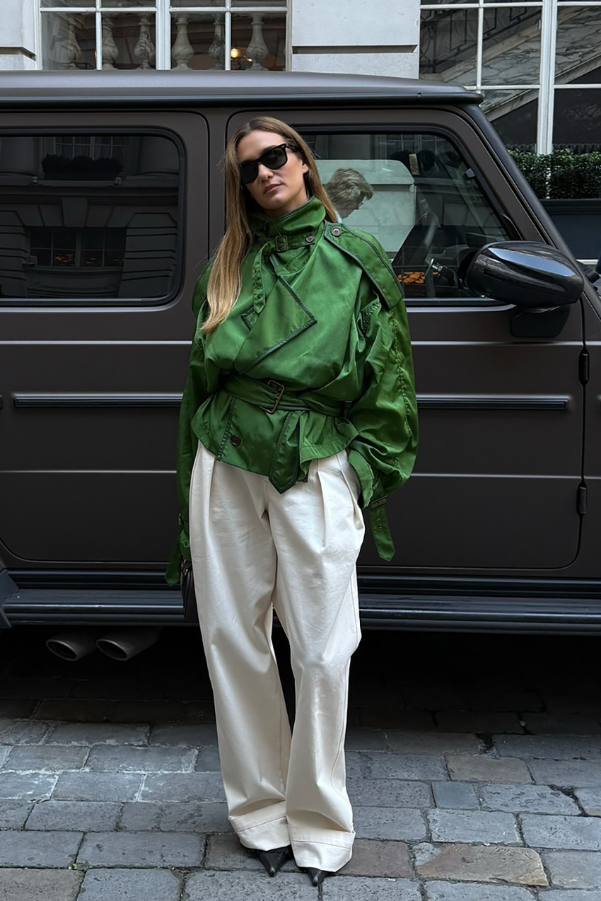 a woman wearing a green cropped trench coat, white pants, and black pointed toe heels