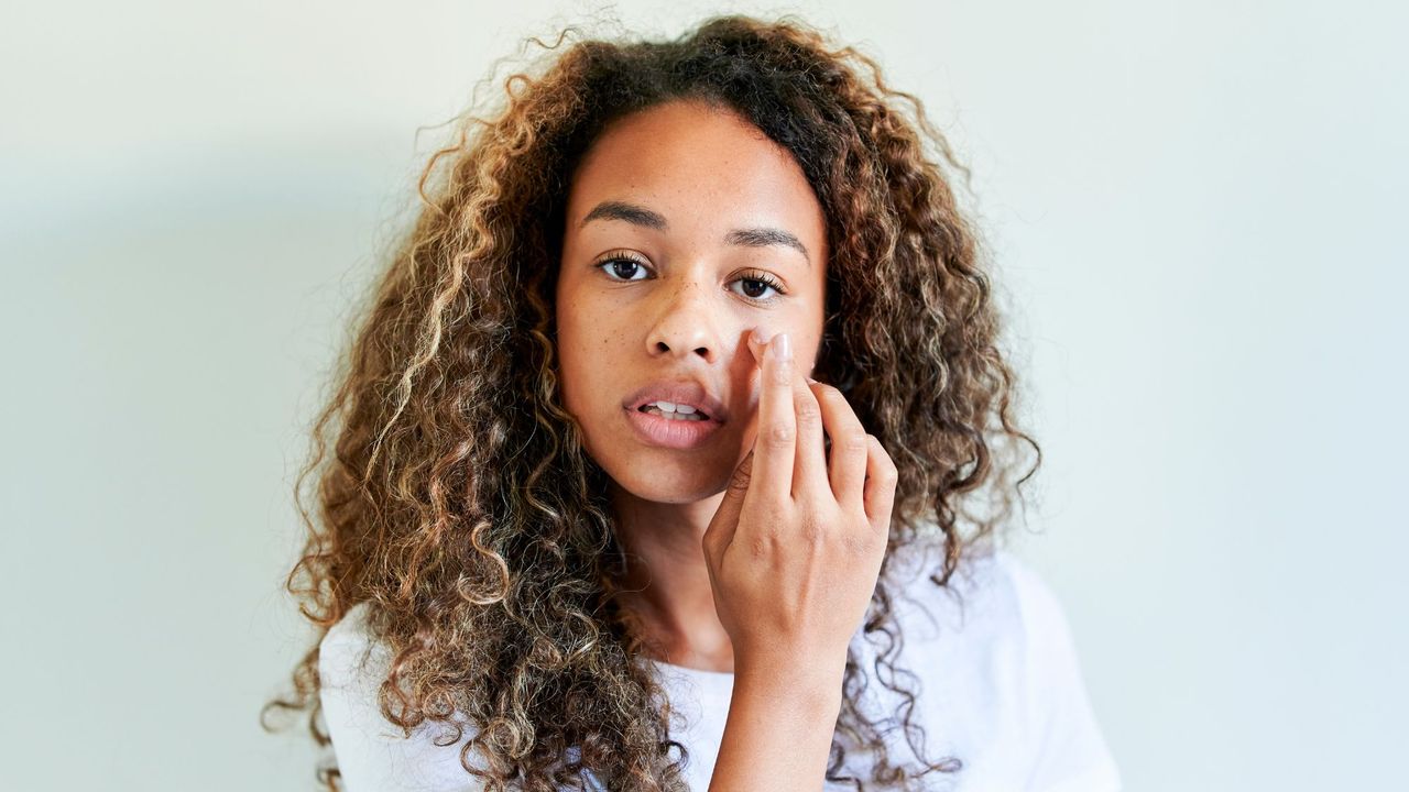 Girl applying skincare product to cover up spot