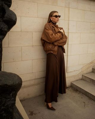 fashion influencer @vivianhoorn wearing a brown leather bomber jacket with a brown maxi dress and Saint Laurent slingback heels