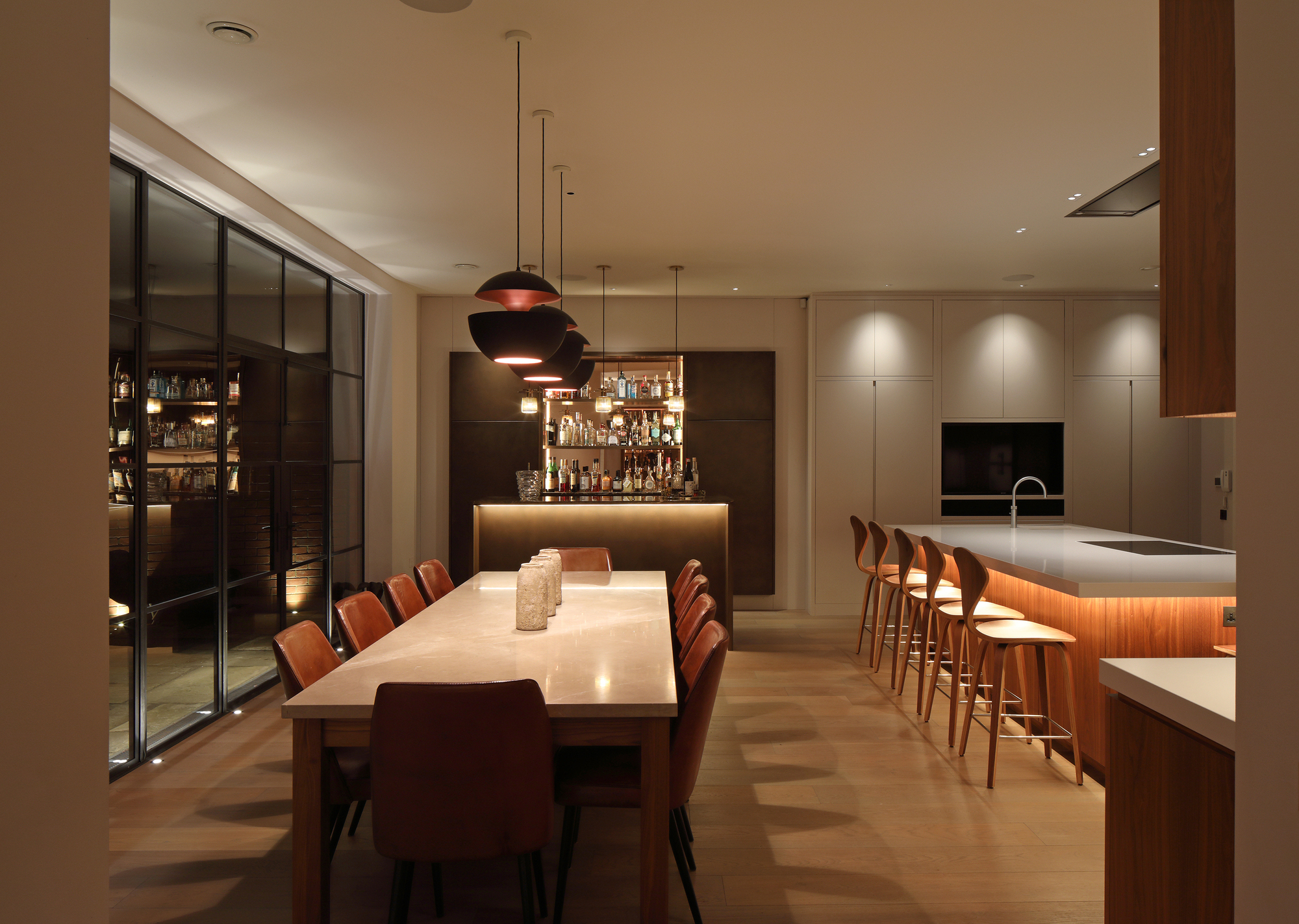 An open play kitchen with a large dining table and a large kitchen island with wall lights, pendant lights, and under counter lighting on the island