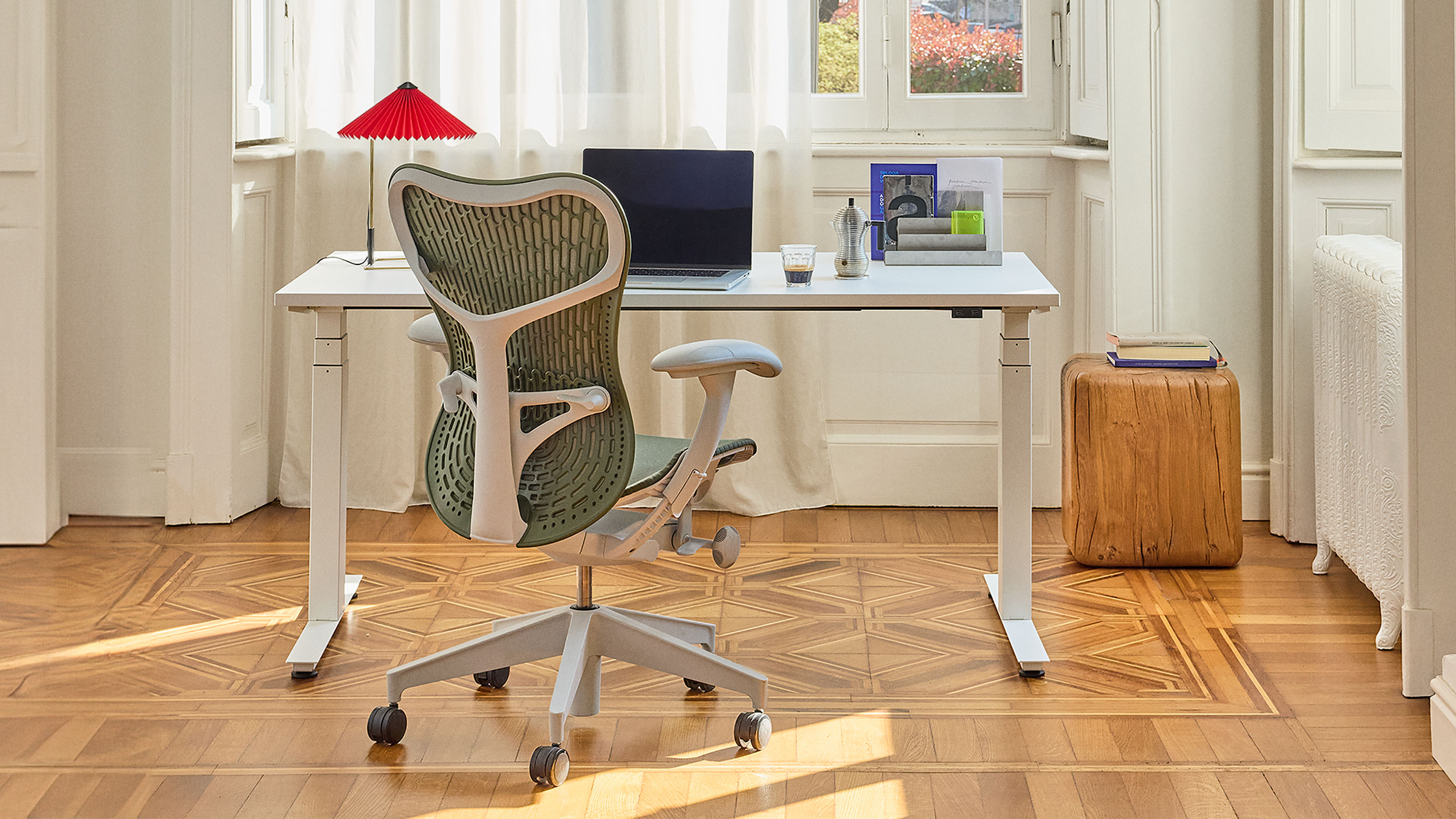 Grey and white office chair sitting at white desk with laptop looking our onto window on sunny day