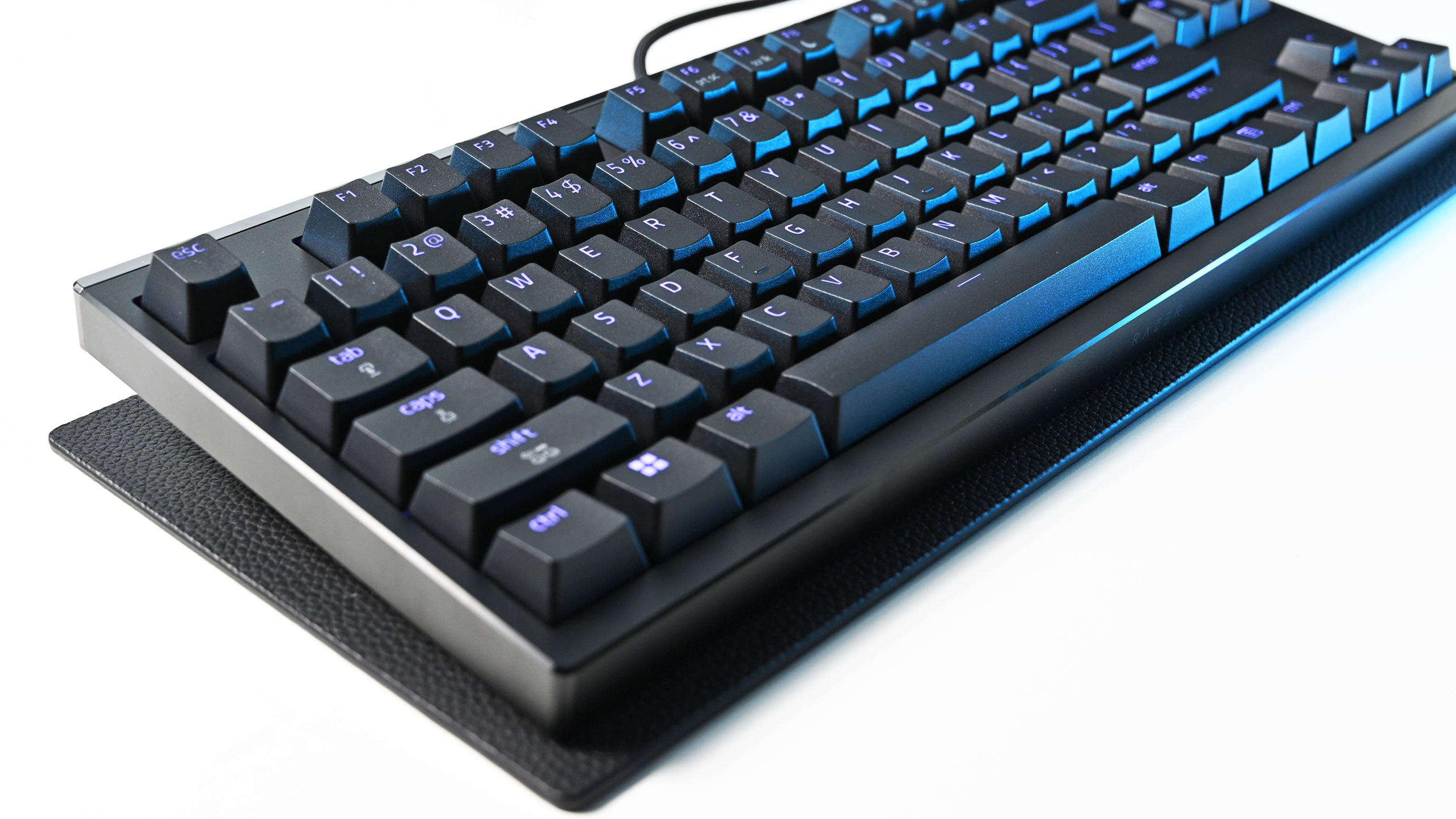 Angled side view of the Razer mechanical keyboard resting on a textured black mat, showcasing its profile and illuminated blue keycaps.