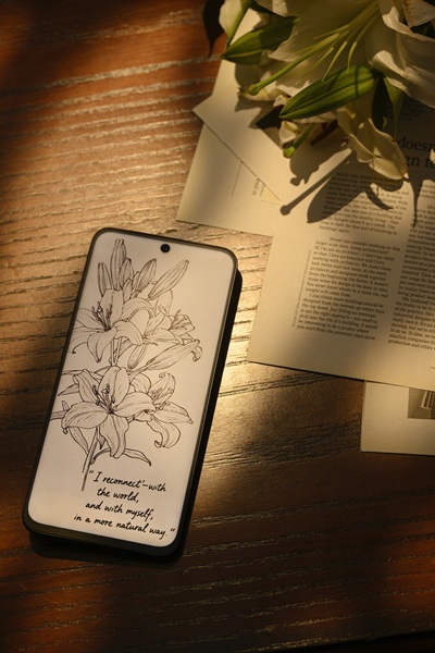A TCL NXTPAPER 60 Ultra lying on a table beside flowers and some scattered papers.